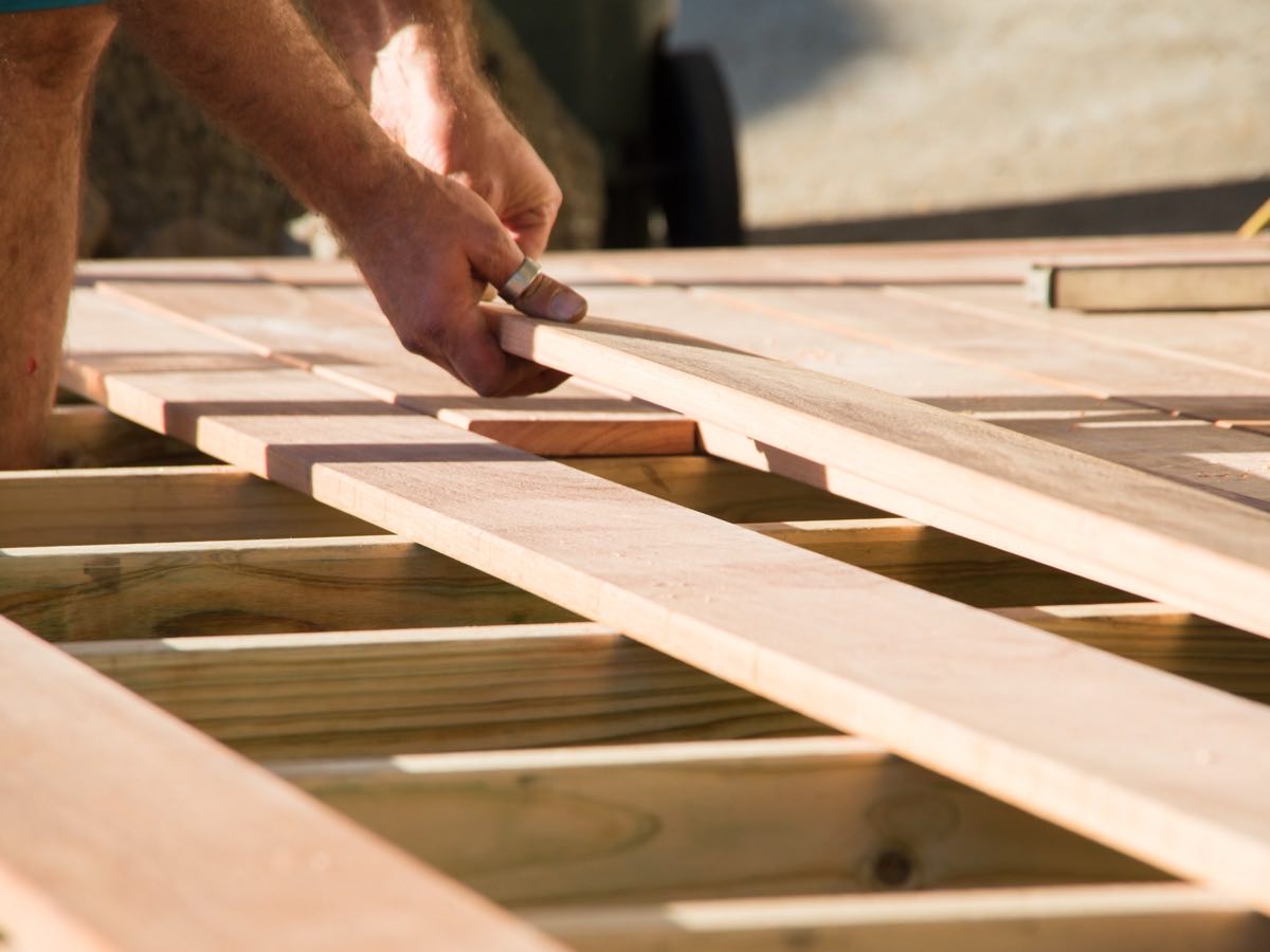 Carpenter fitting deck boards across newly framed pressure-treated joists