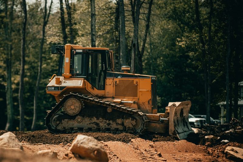 Yellow tracked bulldozer with its blade down on cleared red clay ground