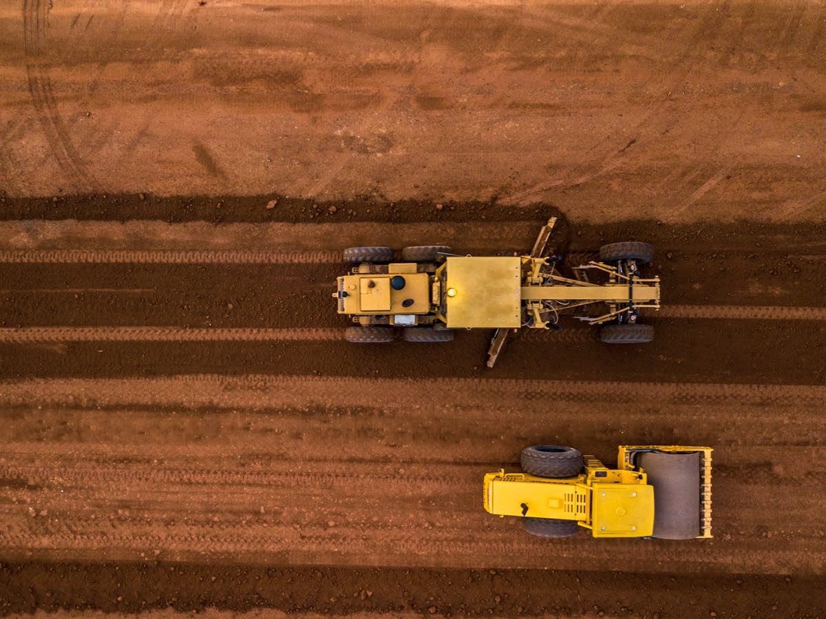 Aerial view of a motor grader and a roller shaping a red clay building pad