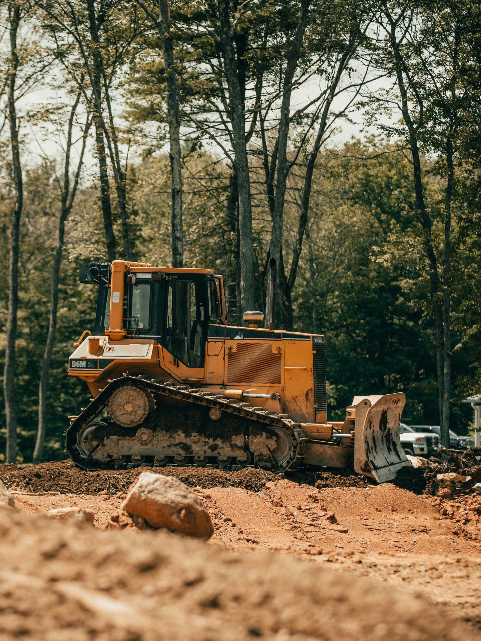 Yellow tracked dozer parked on a cleared lot of red clay and spoil piles, green treeline behind it, on a job near Lake Norman, North Carolina