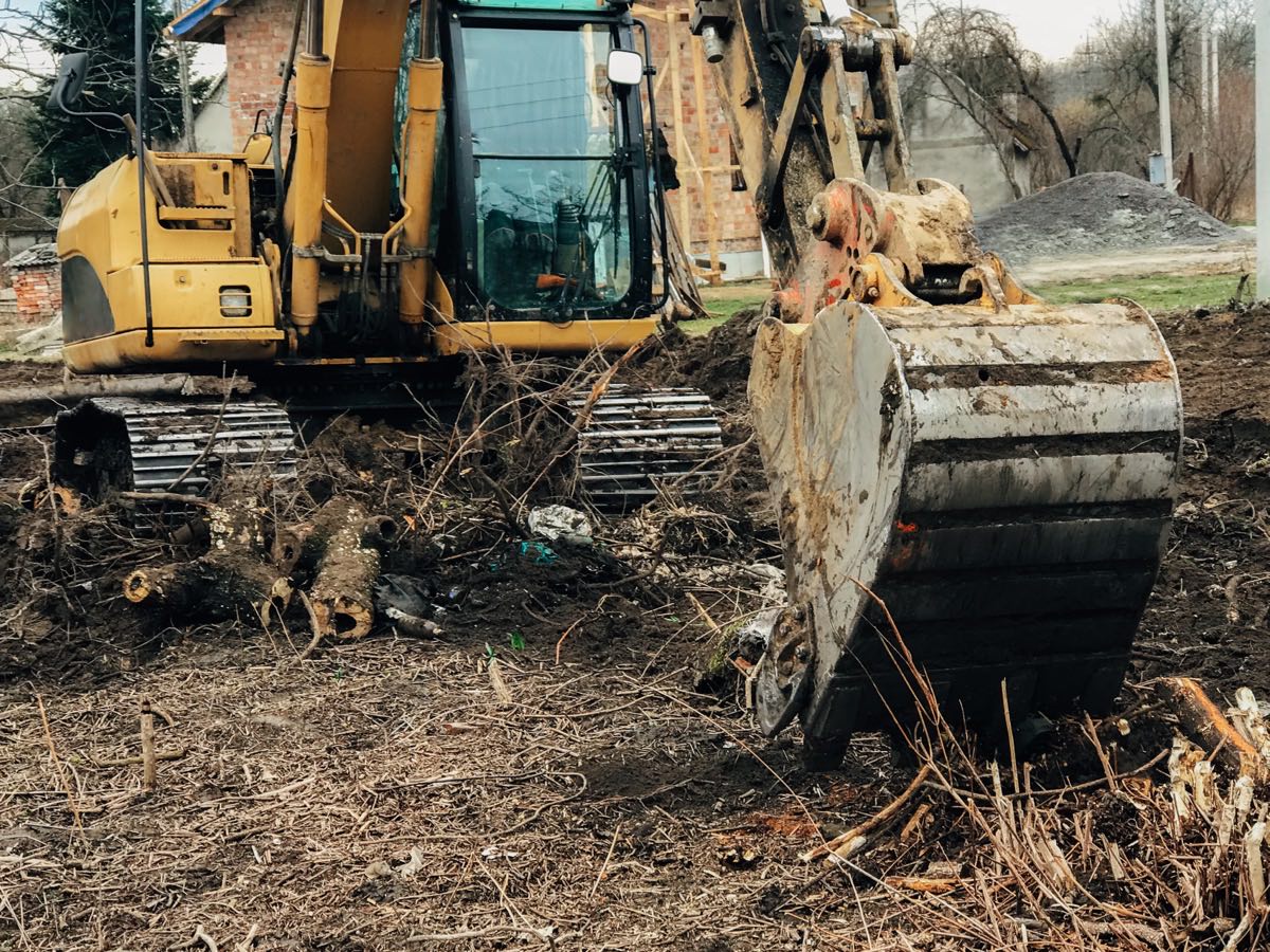 Tracked excavator with a grapple bucket pulling brush and stumps off an overgrown lot