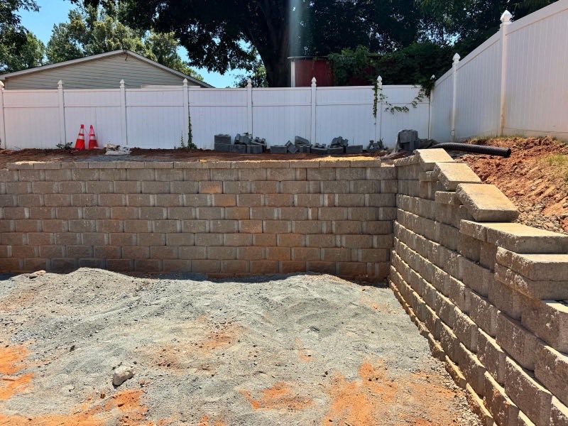 Block retaining wall part-built with a compacted stone base in front of it