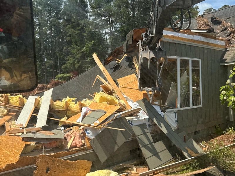 Excavator pulling apart a structure with broken timber and debris piled below