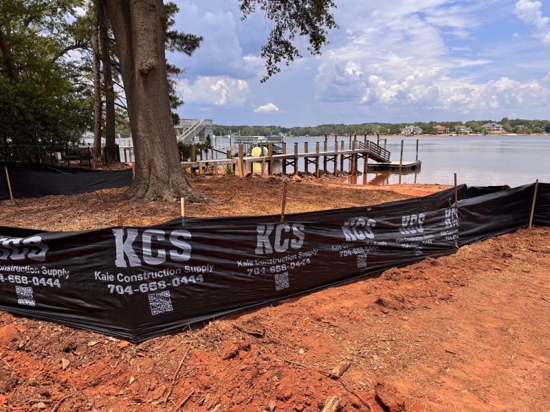 Silt fence staked along the downhill edge of a lakefront lot with the water behind