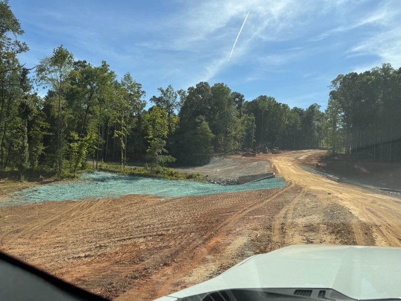 Graded access road and shoulder with a green hydroseed tint across the bare soil