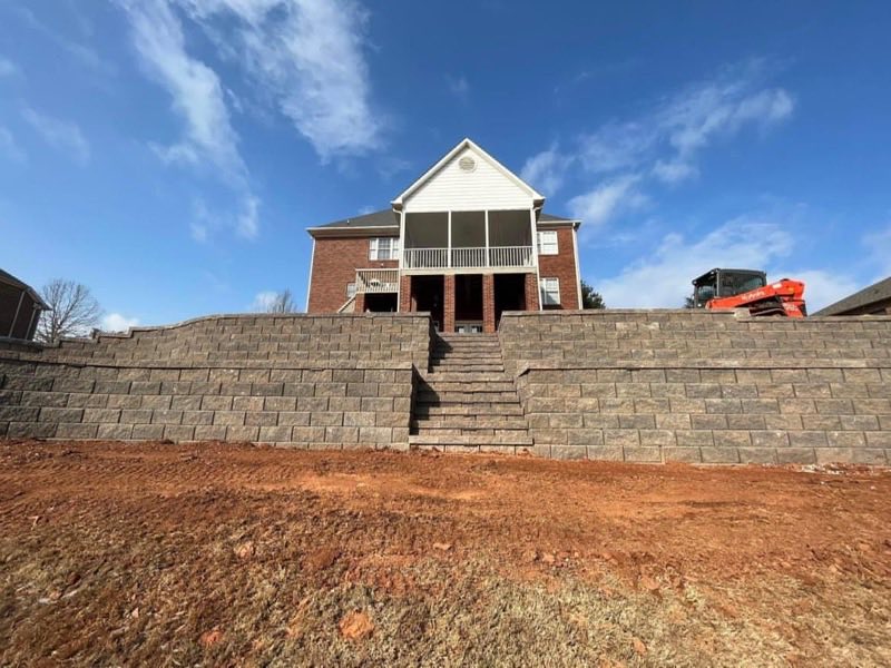 Long block retaining wall with a set of steps leading up to a house