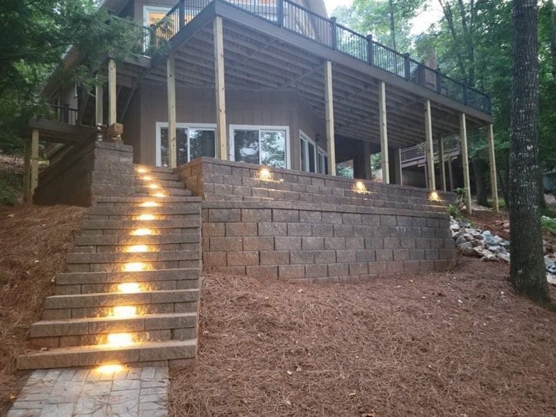 Retaining wall with lit stone steps running up to a deck at dusk