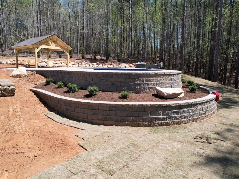 Curved block retaining wall enclosing a pool and pergola in a wooded setting