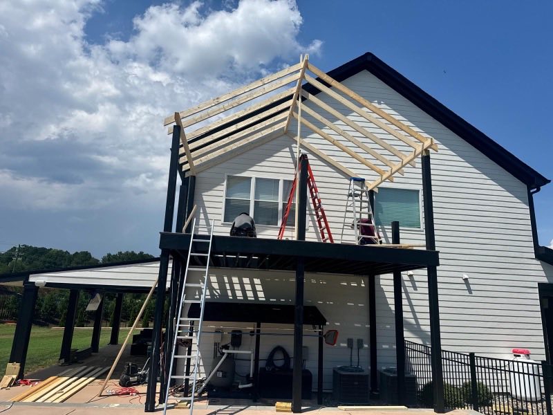 Deck and porch roof framing on black steel posts at the rear of a house